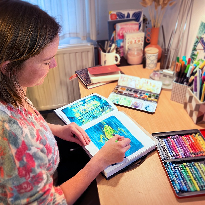 Sophie Bortier en train de dessinée une grenouille aux pastel à la cire sur son bureau